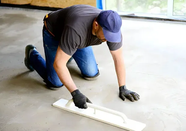 Worker using a straightedge to finish a concrete floor slab