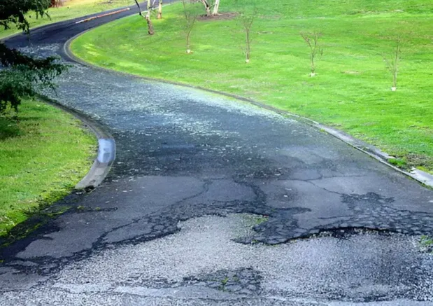 Eroded and cracked asphalt driveway beside grass